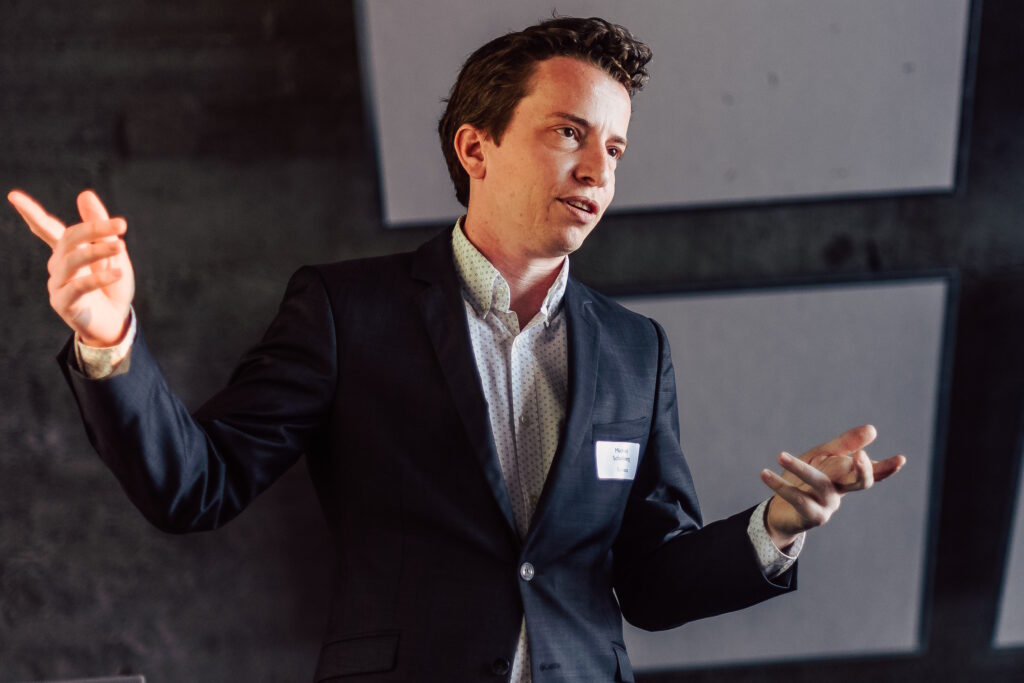 Michiel Scholberg presents at the Future Is WOW wearing a white shirt and black suit.