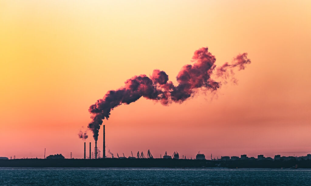 Emissions from a chimney at a manufactuing plant with sunrise in the background.