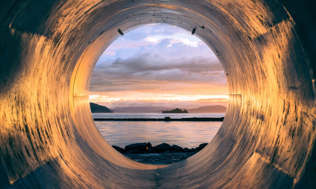 Looking through a storm drain out to sea at sunset with islands in the background.