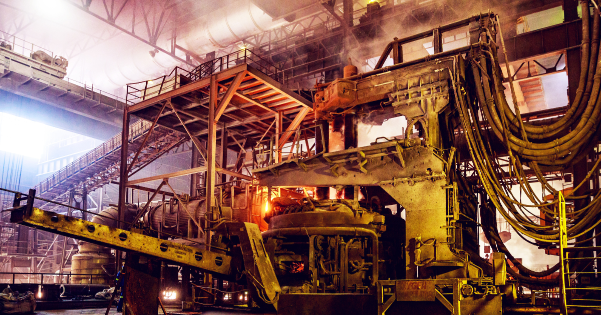 A blast arc furnace in a steel manufacturing facility. Some fire visible, and some smoke.